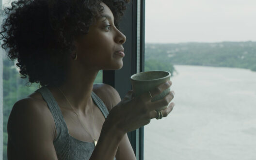 A woman having a cup of tea and viewing a river view from window