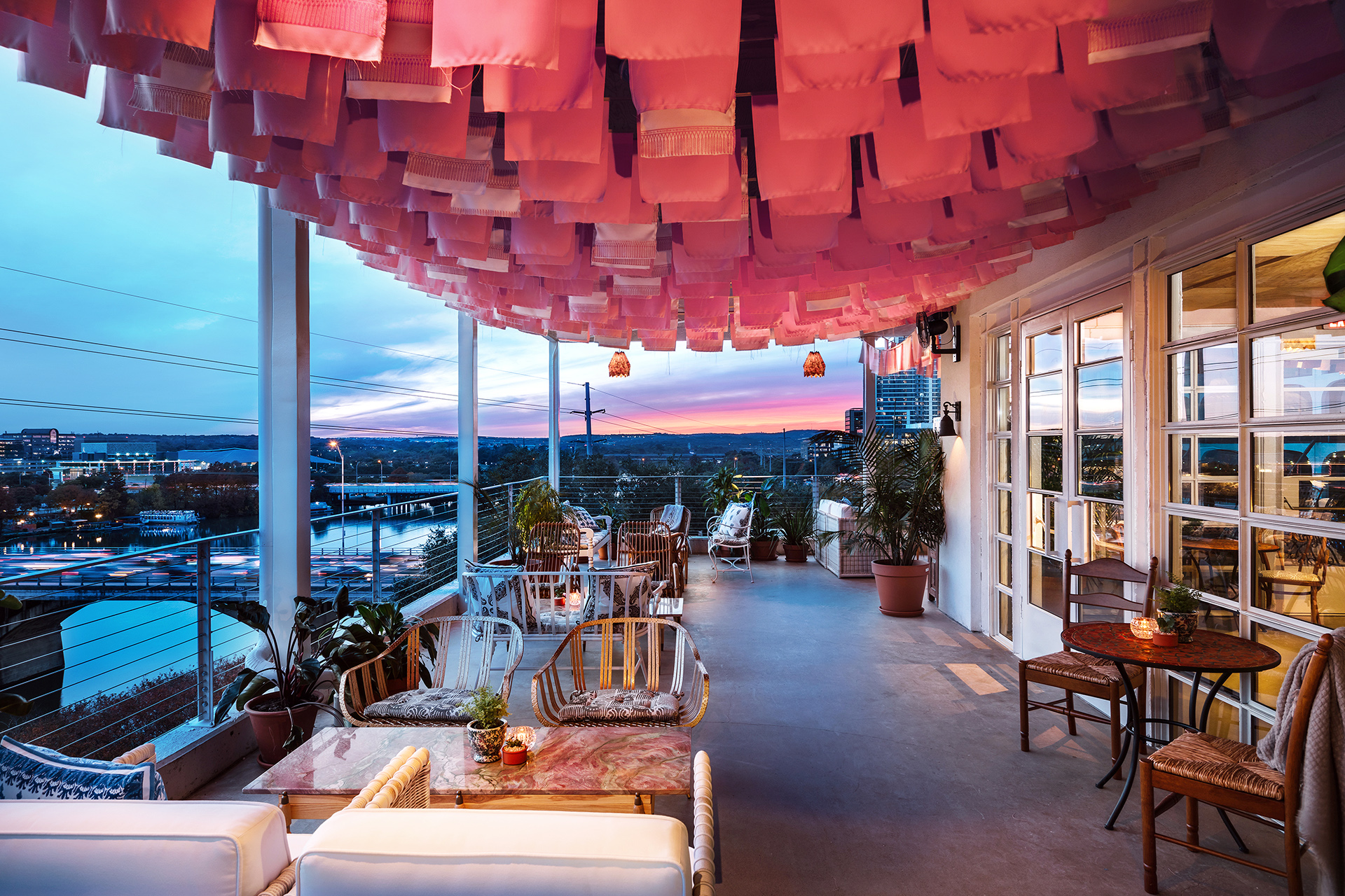 A patio area with tables, chairs, and lanterns overlooking a cityscape at sunset.