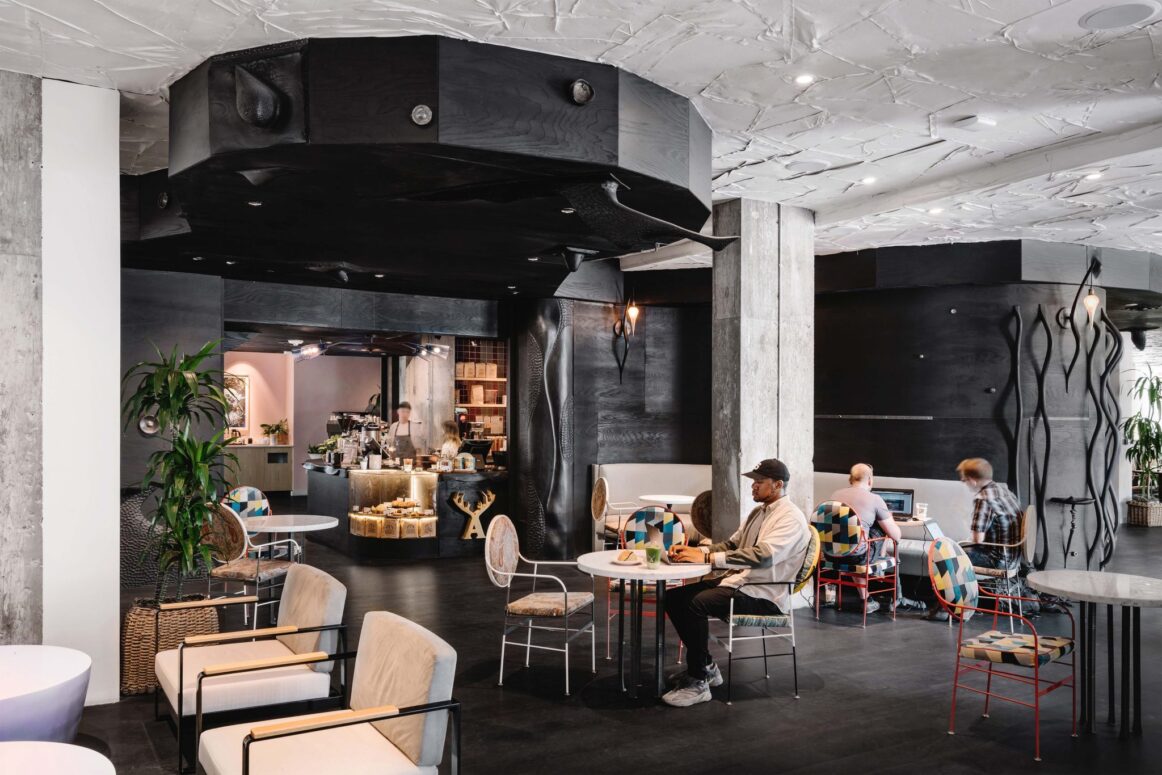 A man sits at a table in front of the coffee shop in a hotel lobby