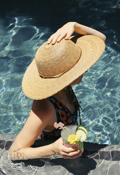 Woman with cap in the swimming pool holding a glass of drink