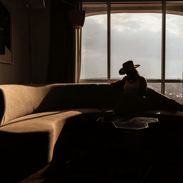 The silhouette of a person in a cowboy hat sitting on a sofa in front of a window with a city view, plus other moody images.
