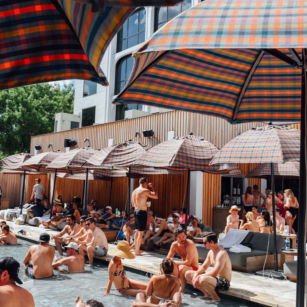 People hang out in a shallow swimming pool surrounded by plaid umbrellas