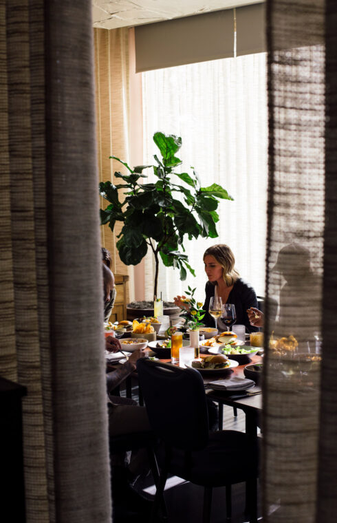 Through a curtain, a woman sits at a private dining table with food at a restaurant