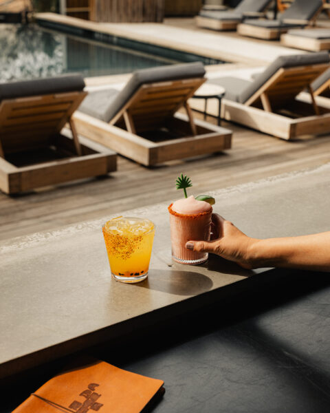 Two rimmed cocktails on a concrete bar ledge by a swimming pool with wooden lounge chairs.
