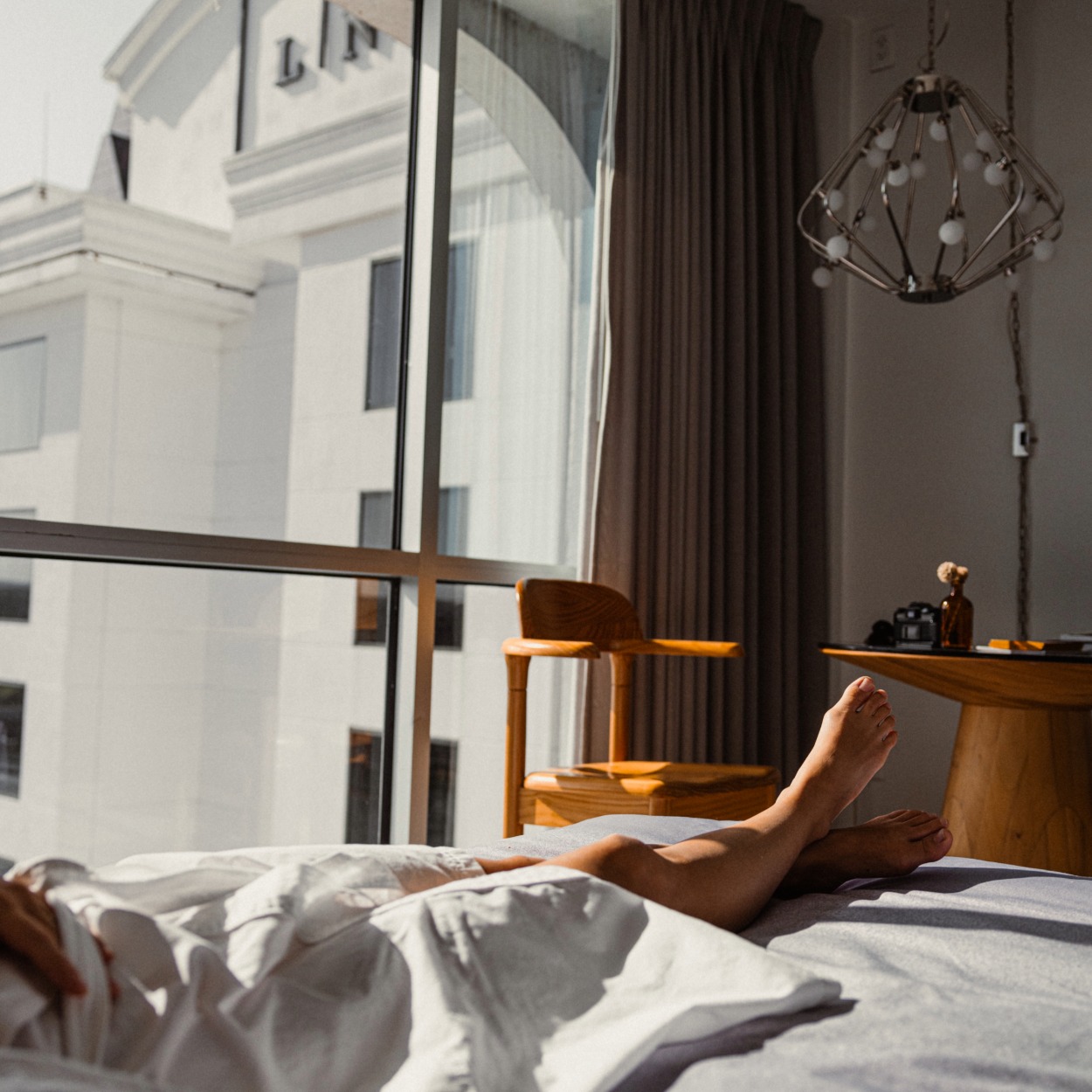 Guest stretched out in bed beside floor-to-ceiling windows in a room at The LINE Austin