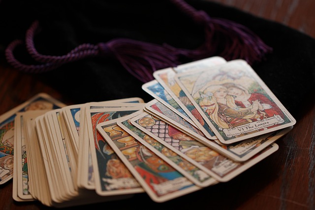 Fanned tarot cards with colorful illustrations beside black pouch on wooden surface, featuring The Lovers