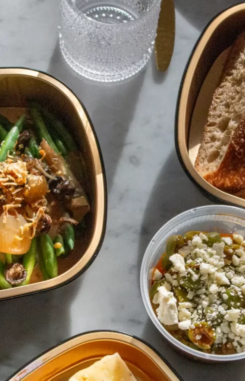A meal spread with green beans, toasted bread slices, feta salad, and lasagna on marble table.