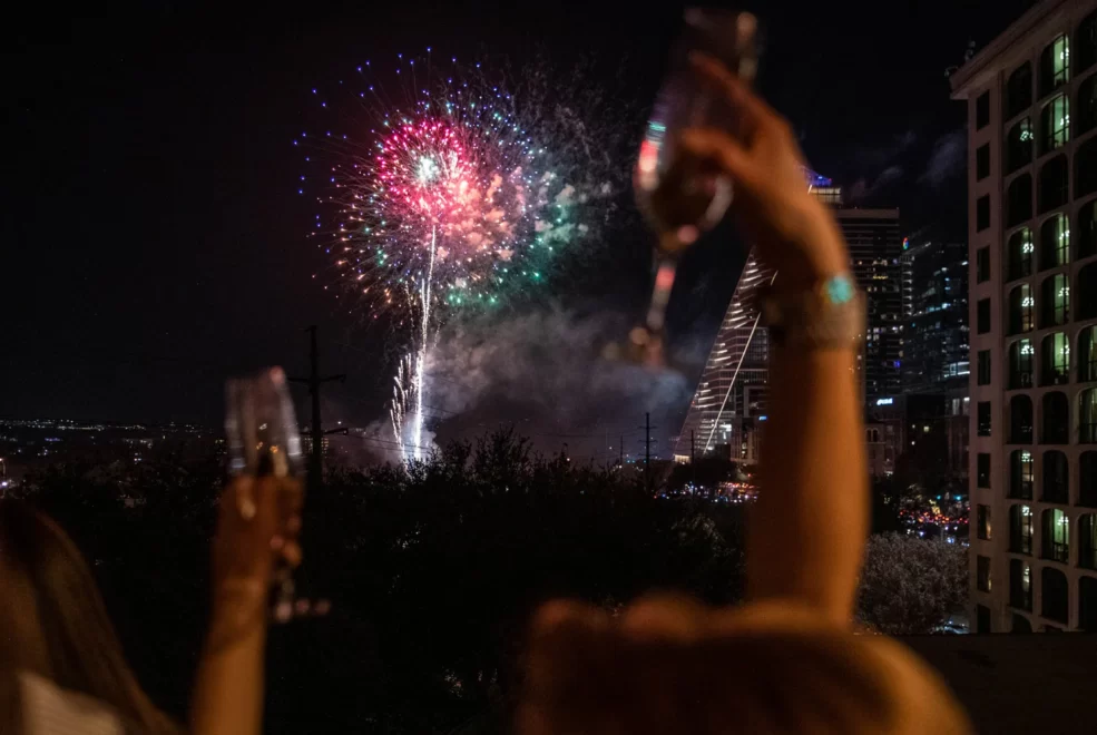 Fireworks over city skyline with people toasting champagne during nighttime celebration