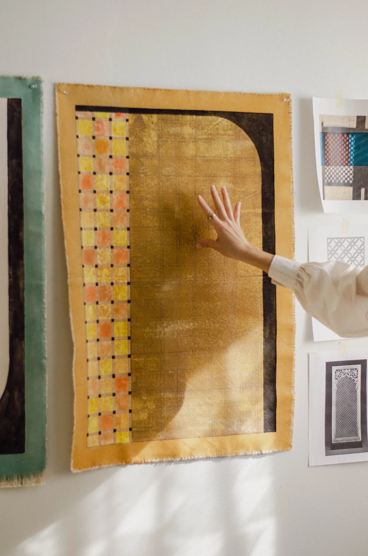 Hand touching textile art with grid texture and bold shapes, surrounded by pinned geometric design sheets