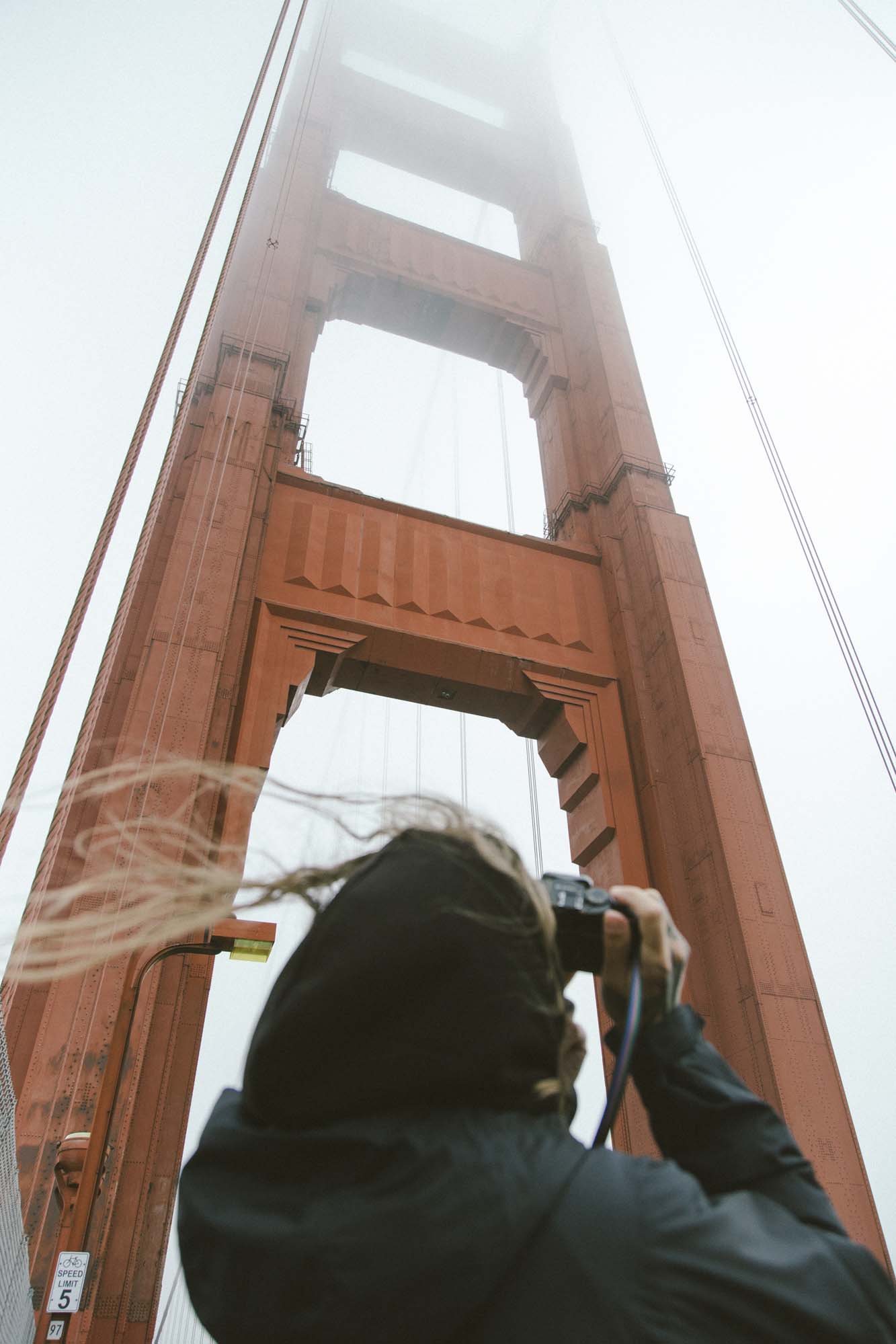 A woman attempting to capture a photo of the "Golden Gate Bridge Tower."