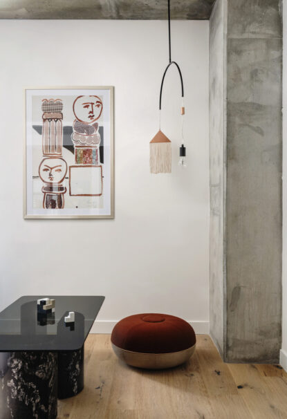A black coffee table, red pouf, and a handmade portrait adorning the wall.