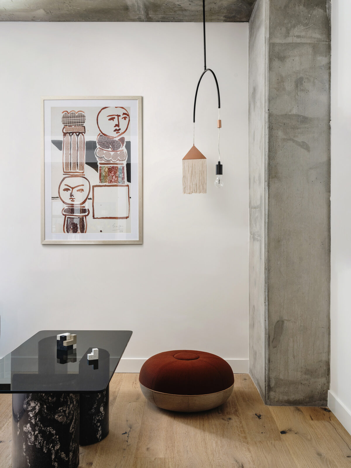 A black coffee table, red pouf, and artwork in the corner of a room