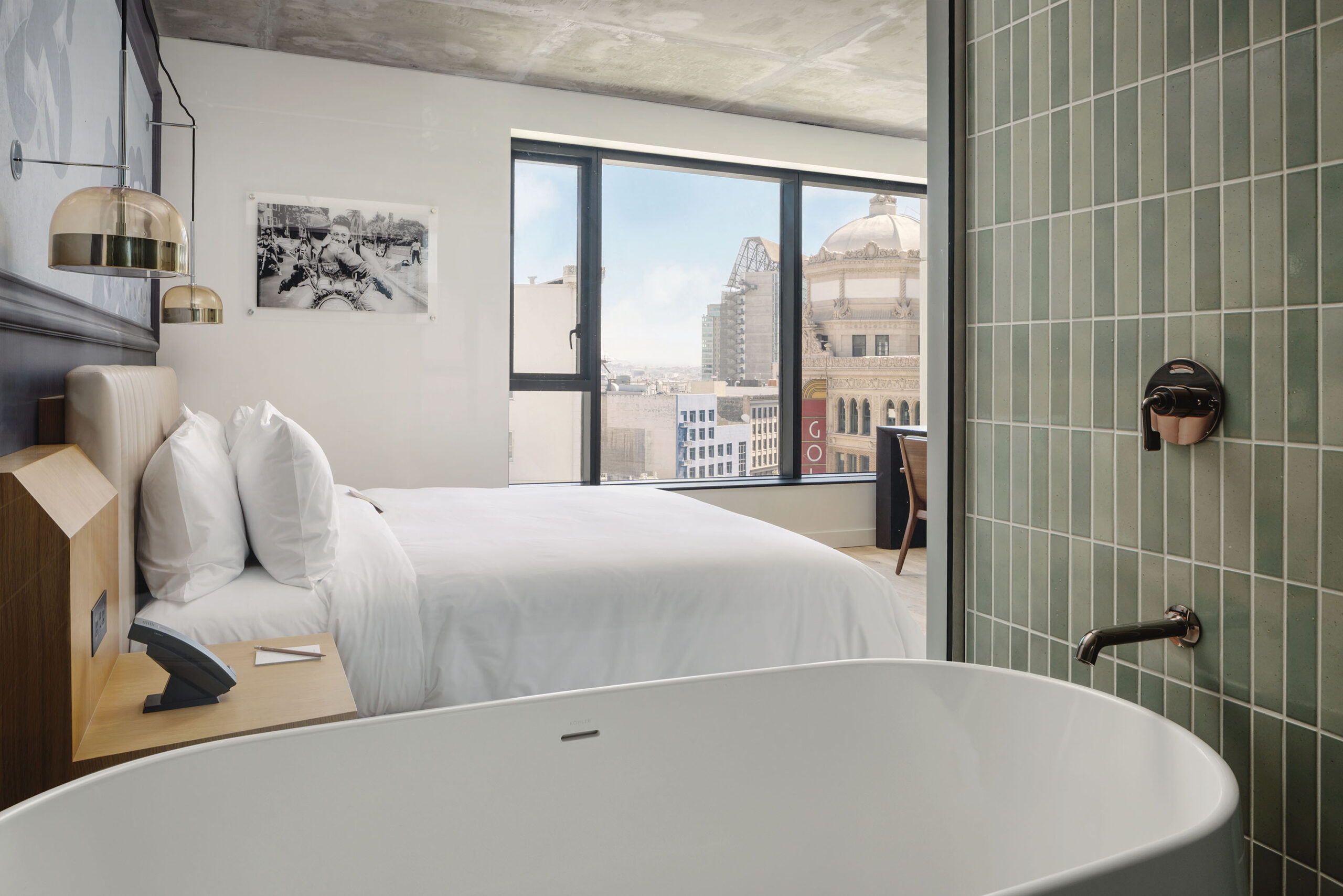 A soaking tub and hotel bed in a room with skyline views
