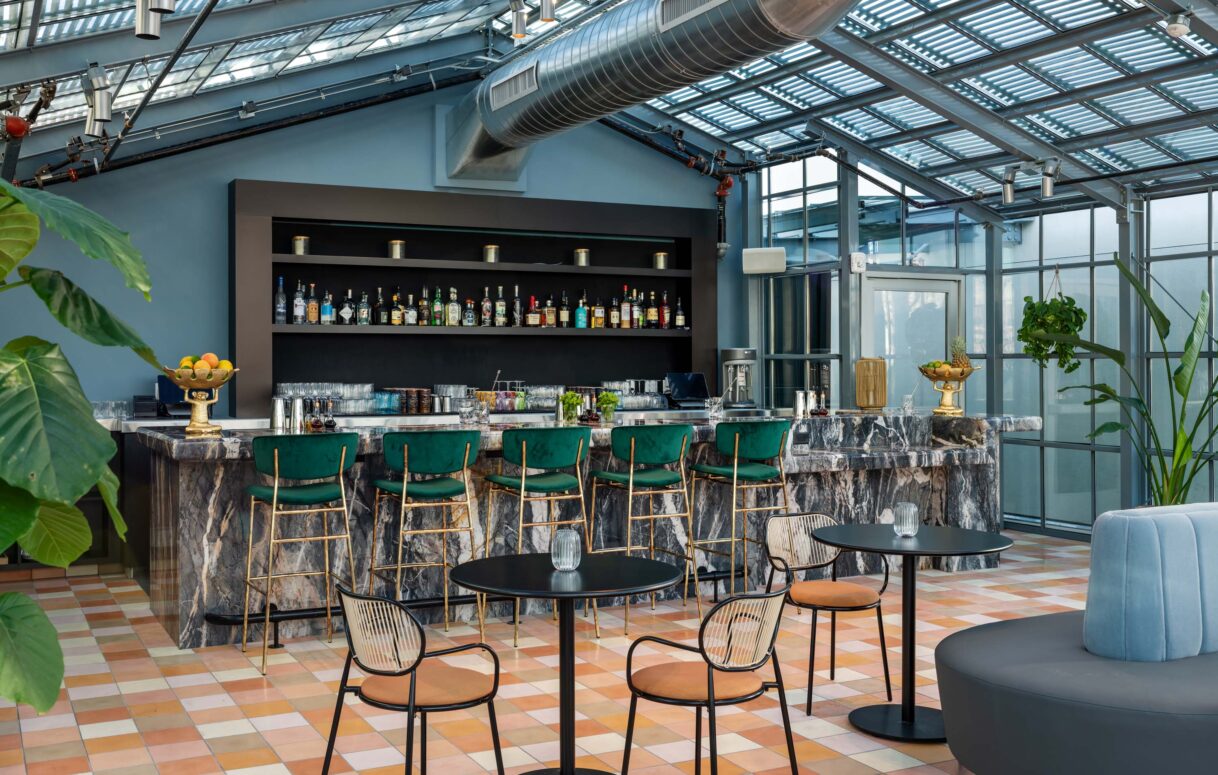Various chairs positioned near the rooftop bar counter, beneath a glass-framed ceiling.