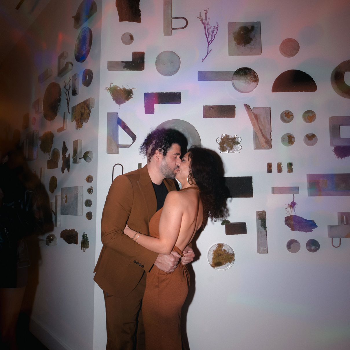 Two people kissing in front of an art installation wall